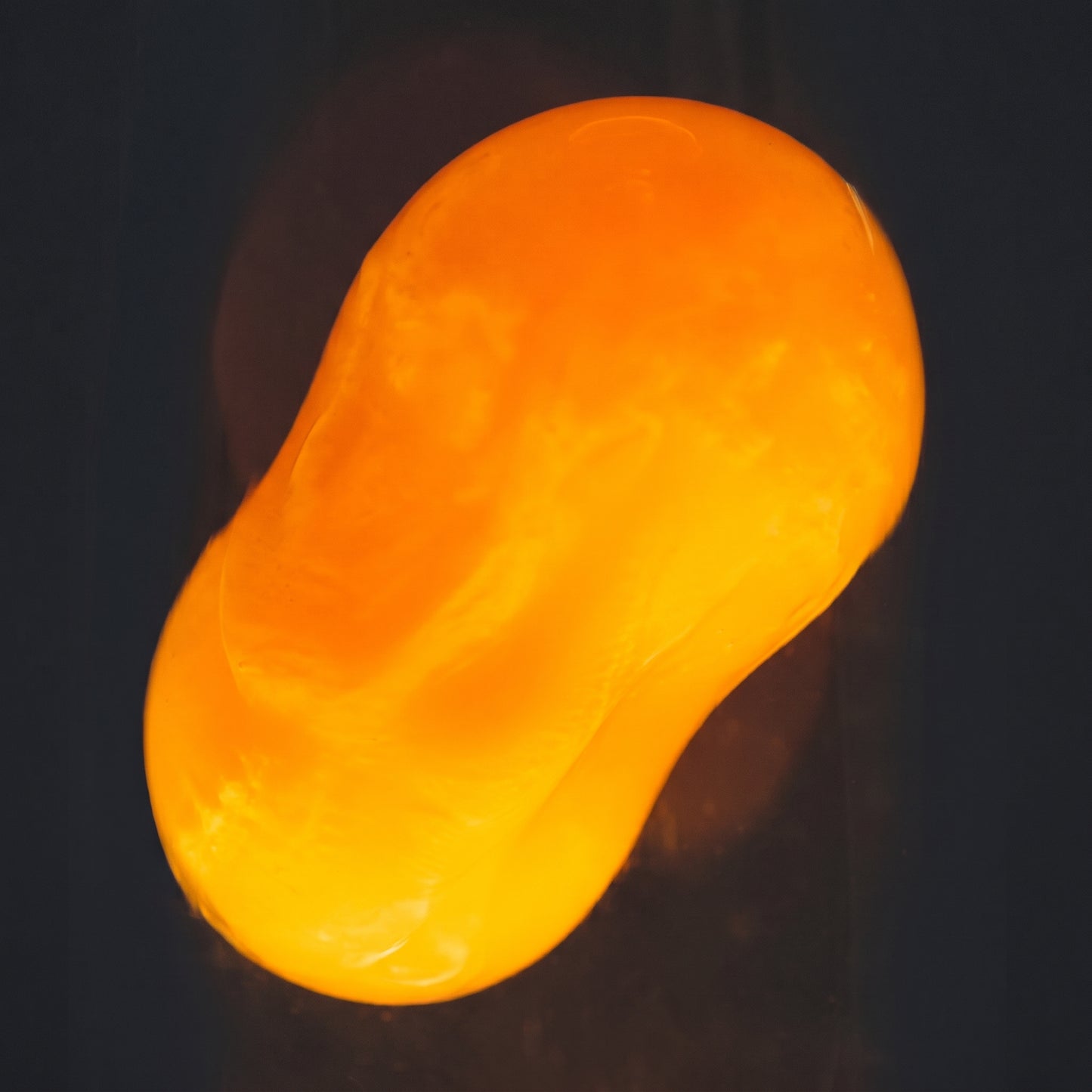 Extreme macro close-up of orange wax blobs floating inside a volcano lava lamp